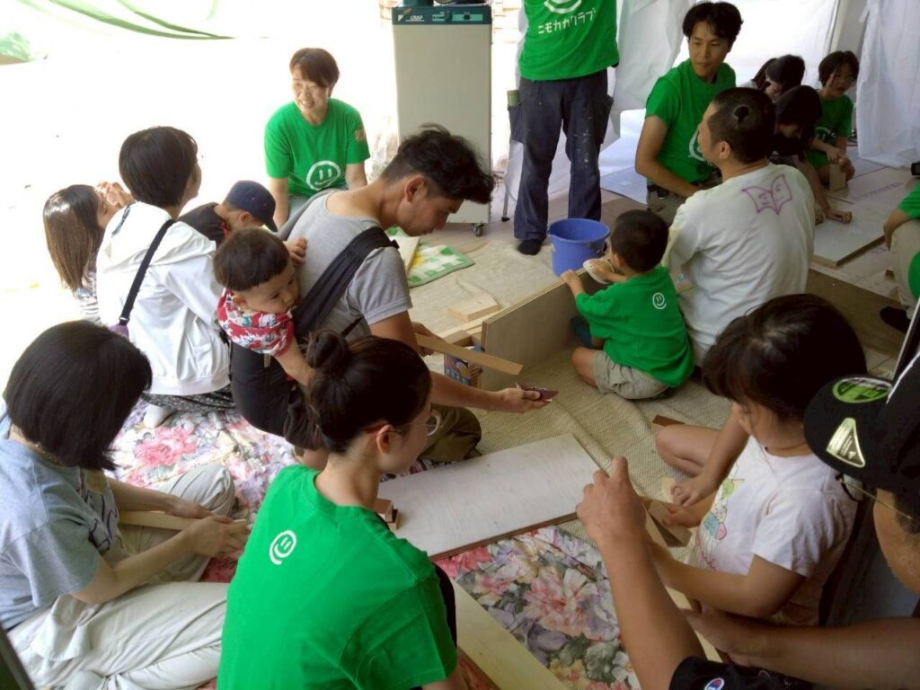 ワークショップで大人と一緒に木を加工する子供たちの写真