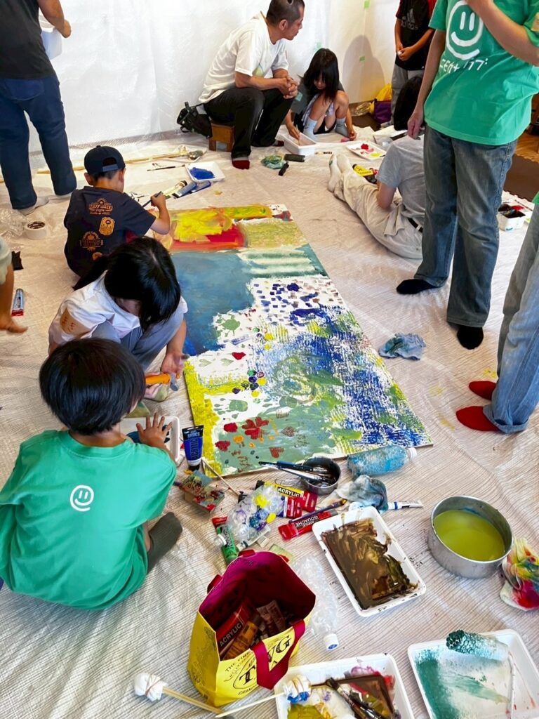 ワークショップで大きな板に絵の具で自由に絵を描いている様子