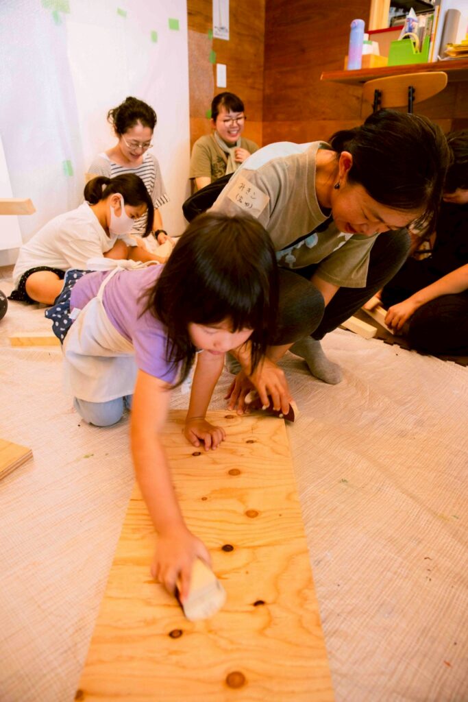 ニモカカのスタッフと保護者の間で木にヤスリをかけている画像