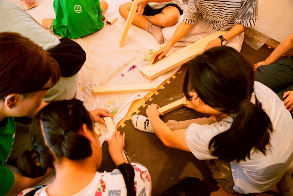 ニモカカのスタッフと子供たちが木にヤスリをかけている画像