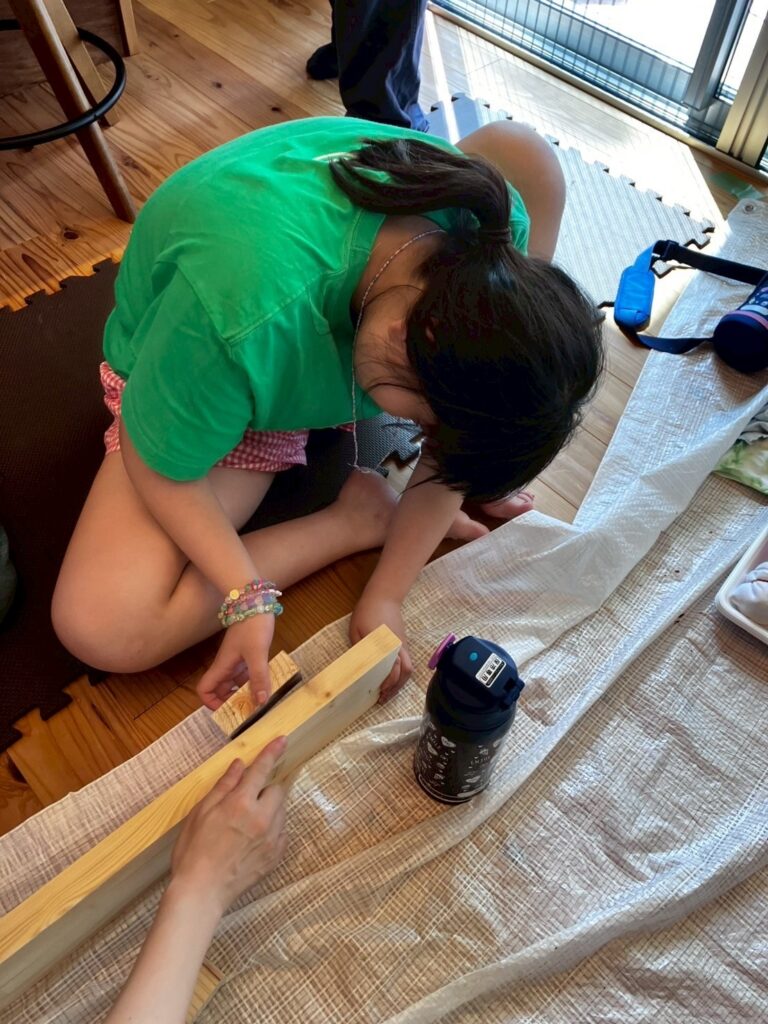 ベンチの木を貼り合わせている子供の写真