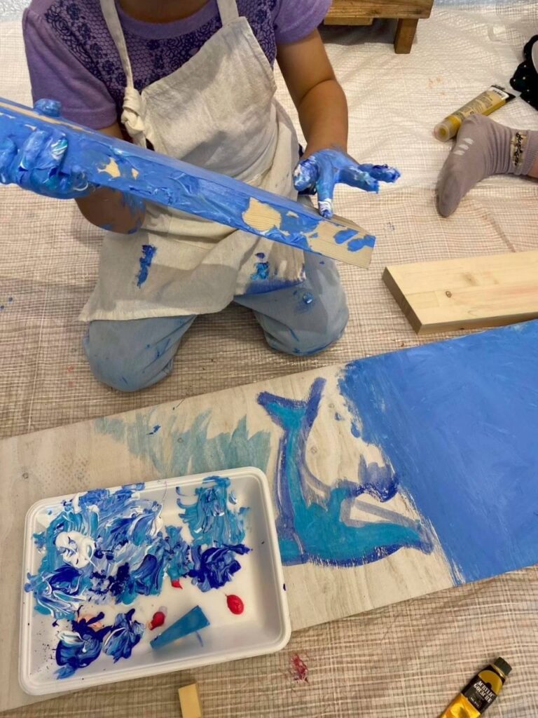 ベンチを作成する木のパーツに素手で絵の具を塗っている風景